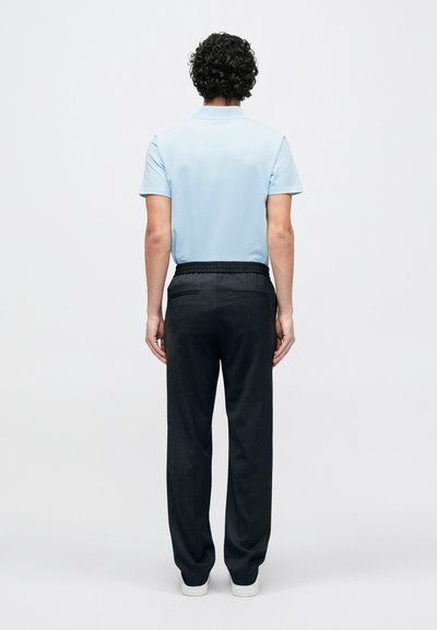 Hele sinine lühikeste varrukatega polosärk, kombineeritud tumeda halli elastse vöökohaga pükstega. Modell on seljaga vaataja poole, minimalistliku taustaga.