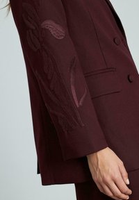 Bordeaux blazer met gedetailleerde paarse bloemenborduursel op de mouw, dubbelgeknoopte uitvoering, zachte textuur en op maat gemaakte pasvorm.
