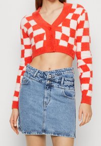 Pull court à carreaux rouges et blancs avec un col en V et trois boutons, associé à une jupe en denim bleu taille haute.