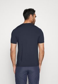 Mornarsko modra majica s kratkimi rokavi v prilagojenem dizajnu, z zaobljenim izrezom in gladko teksturo, z vidnimi ramenskimi šivi.