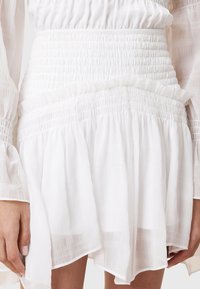 White dress with a textured, tiered design. Features smocked waist and flowing, lightweight fabric with subtle ruffles along the hem.