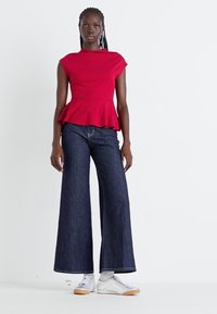 Rød peplum topp med korte ermer, kombinert med mørk blå vide jeans. Sneakers med hvit overdel og lys brun såle.