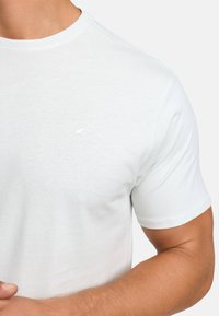 T-shirt a maniche corte azzurro chiaro in cotone morbido. Presenta un logo goffrato discreto sul lato sinistro del petto. Collo tondo e vestibilità regolare.