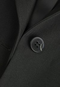 Tessuto nero di un blazer con una vista ravvicinata di un bottone nero lucido e rotondo, caratterizzato da quattro fori e un motivo sottile.