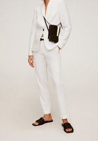 Blazer blanco entallado, pantalones ajustados a juego y sandalias cuadradas de color marrón oscuro. Pequeño bolso negro de bandolera con correa. Texturas suaves.