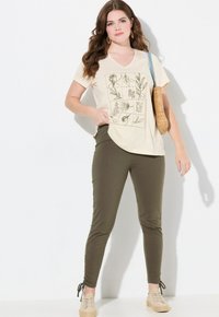 Beige V-ringad t-shirt med botaniskt tryck och text, i kombination med olivgröna slim-fit byxor med dragsko vid anklarna. Espadrillos.