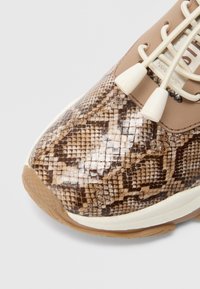 Baskets avec un motif texturé en peau de serpent dans des nuances de brun et beige. Dotées d'une semelle crème et d'accents de laçage crème.