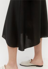 Sort, lette midi-kjole med en buet nederdel, der har en let og luftig stof. Kombineret med lyse beige slip-on loafers.