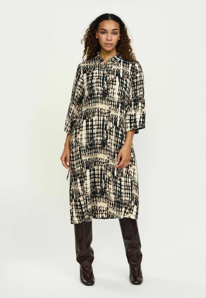 Mustade ja kreemjade mustritega midi kleit krae, kolmeveerand-sleeve'idega ja vabalt langev, koos vormitud pruunide põlvekõrguste saapaid.