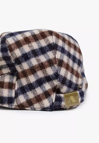 Cappello di lana a quadri nei colori crema, marrone e blu navy con una finitura testurizzata e un'etichetta in ottone sul lato. Motivo a quadri distintivo con design arrotondato.