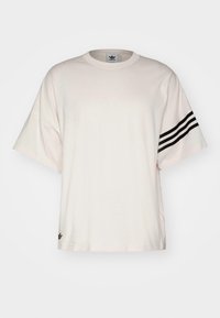 Ljusbeige bomulls t-shirt med rund halsringning, korta ärmar och tre svarta ränder på vänster ärm. Litet logo vid fållen.
