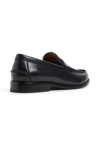 Schwarze Lederloafer mit niedrigem Absatz, die ein elegantes Design und detaillierte Steppnähte entlang der Nähte und der oberen Kante aufweisen.