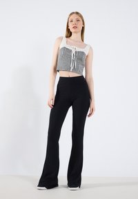 Pantalones negros acampanados de canalé combinados con un top recortado a cuadros que presenta un escote cuadrado y un detalle de lazo en la parte delantera.