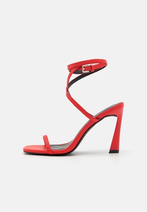 Red leather high-heeled sandals with a strappy design, adjustable ankle buckle, and a sleek, tapered heel. Smooth texture and minimalist style.