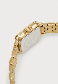 Montre rectangulaire dorée avec une finition poli, dotée d'un cadran blanc lisse et d'un bracelet en métal à maillons, incluant une couronne pour le réglage.