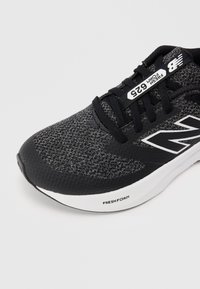 Chaussure de course noire et grise avec une tige en tissu texturé, comportant un logo "N" blanc et "FRESH FOAM" sur la semelle pour un amorti.