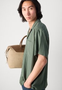 Green short-sleeve shirt with a textured pattern, single chest pocket, paired with a beige bag featuring brown accents and top handles.