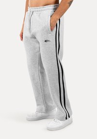 Grijze sweatpants met zwarte zijstrepen, voorzien van een elastische tailleband en een logo-accent. Gecombineerd met witte sneakers.