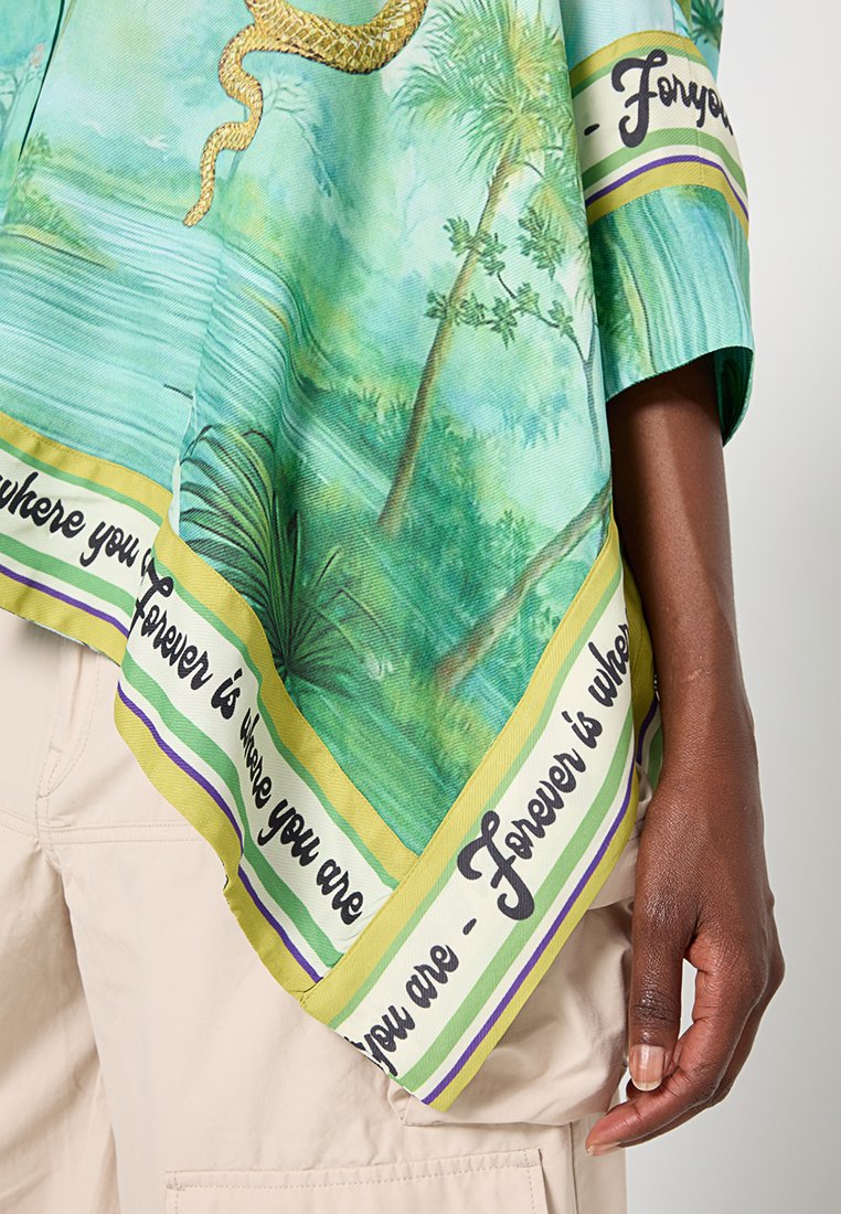 Luźna zielona tunika z motywem roślinnym i złotym wężem. Dół wykończony jest wzorzystą bordiurą oraz czarnym napisem.