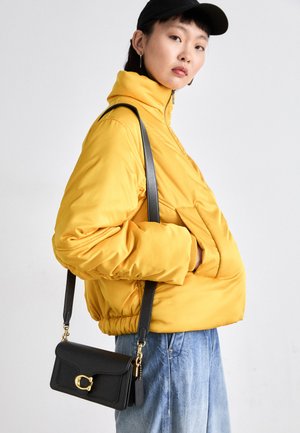 Yellow padded jacket with high collar and front pocket, paired with a black crossbody bag featuring gold hardware. Casual denim bottoms.