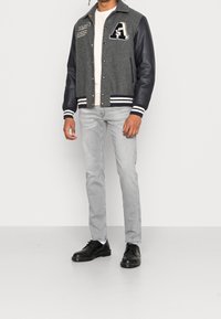 Grå ullblandad varsityjacka med svarta lädersleeves, randiga manschetter och broderat bokstavsaccent. Bärs med ljusgrå jeans och svarta skor.