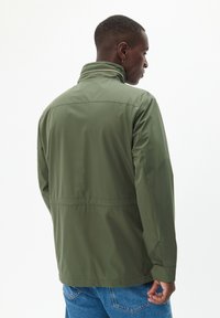 Grüne, leichte Jacke mit hohem Kragen, wasserabweisendem Stoff, Reißverschlussöffnung und elastischen Bündchen. Hat eine glatte Textur und ein schlichtes Design.
