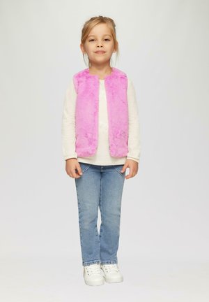 Roze nepbont vest gedragen over een lange mouw witte top, gecombineerd met blauwe jeans en witte sneakers. Kind staat rechtop met een neutrale uitdrukking.