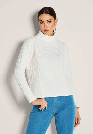 Weißer Rollkragenpullover mit strukturiertem Zopfmuster, langen Ärmeln und lockerer Passform, kombiniert mit blauen Jeans.