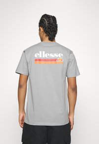 Gray t-shirt featuring a large white "ellesse" logo on the back, accompanied by horizontal orange and red stripes. Short sleeves, casual cut.