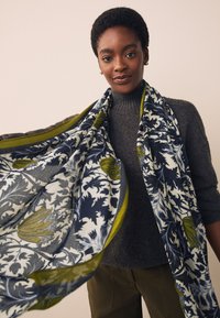 Écharpe à motif floral en bleu marine, blanc et vert olive. Fabriquée en tissu léger à texture lisse ; elle présente une bordure contrastante.