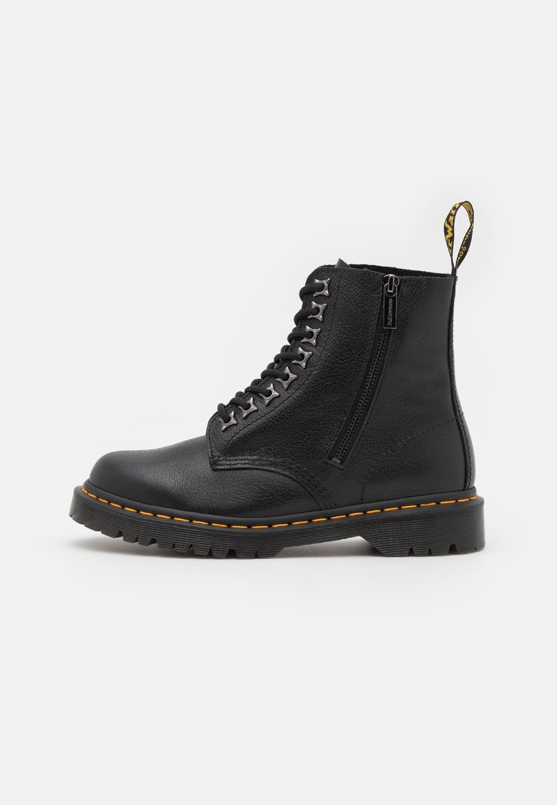 Bottine noire en cuir à lacets avec fermeture éclair sur le côté, semelle épaisse à crampons, surpiqûres jaunes et languette marquée à l'arrière.