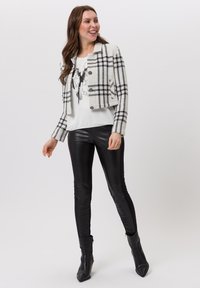 Schwarz-weiße kariertes, kurzes Jacket aus strukturiertem Stoff, kombiniert mit einem grafischen weißen T-Shirt und eleganten schwarzen Lederhosen sowie Stiefeletten.