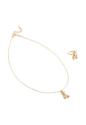 Goldenes Halsketten- und Ring-Set, jeweils mit einem kleinen polierten Teddy-Bär-Anhänger an einer feinen Kette und einem Band vor einem weißen Hintergrund.