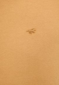 Beige cotton fabric with a soft texture, featuring a small, embroidered horse logo in the top left corner.