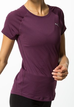 Close-up van een persoon die een nauwsluitend paars Puma sportshirt met korte mouwen draagt, met het Puma-logo op de borst.