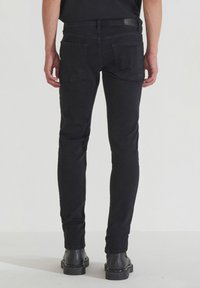 Jeans de mezclilla negra con un diseño ajustado, dos bolsillos traseros y un parche de cuero en la cintura, combinados con botas negras de suela gruesa.