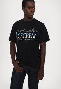 Black cotton t-shirt featuring a skyline graphic in blue and white, with "ICECREAM" text and "LONDON UNITED KINGDOM" printed below.