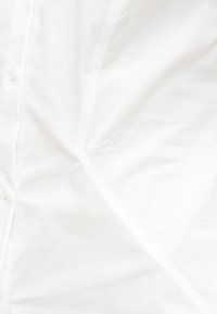 Tissu de chemise blanche à boutons avec une couture diagonale subtile et de faibles initiales brodées sur le devant.