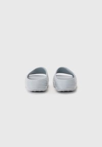 Sive slip-on cipele s rebrastom teksturom i otvorenom stražnjom stranom, s glatkim gornjim dijelom i ravnim, protukliznim potplatom. Minimalistički dizajn.
