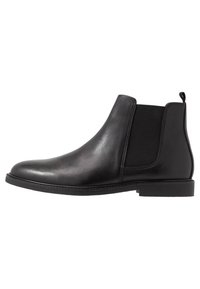 Botas Chelsea de cuero negro con paneles elásticos a los lados, puntera redondeada y suela baja de goma. Incluyen una lengüeta en el talón para facilitar el calzado.