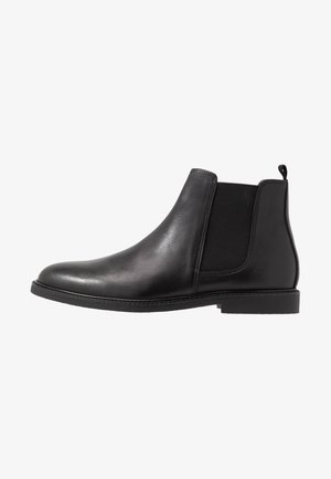 Botas Chelsea de cuero negro con paneles elásticos a los lados, puntera redondeada y suela baja de goma. Incluyen una lengüeta en el talón para facilitar el calzado.