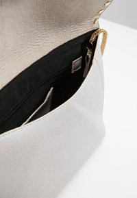 Vitt läderhandväska med en strukturerad yta, en guldkedjeaccent och ett svart tyginteriör med en zippered ficka och kortslot.