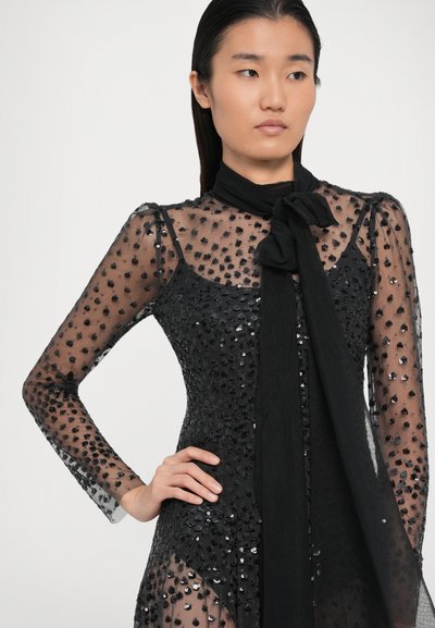 Musthave mustrassz mustrasssid tükk langenud varrukatega must sädelev kleit, millel on kergelt läbipaistvad detailid ja sõlme sidumine kaela piirkonnas. Omab tekstuurilisi detaile ja keha lähedal istuvat siluetti.