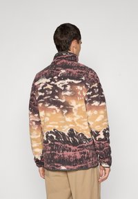 Fleecejack van een multicolore berg- en hemelpatroon in paarse, oranje en roomkleurige tinten; hoge kraag en lange mouwen.