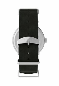 Ura Timex z okroglim ohišjem iz srebrnega nerjavečega jekla, črnim usnjenim trakom in srebrno zaponko. Ima vidne šive in luknje za nastavitev.