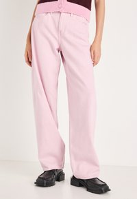 Rozā džinsa platās kājas bikses ar brīvu piegriezumu. Gluda tekstūra. Kombinētas ar melniem apaviem ar reljefa zoli un apaļu purngalu.