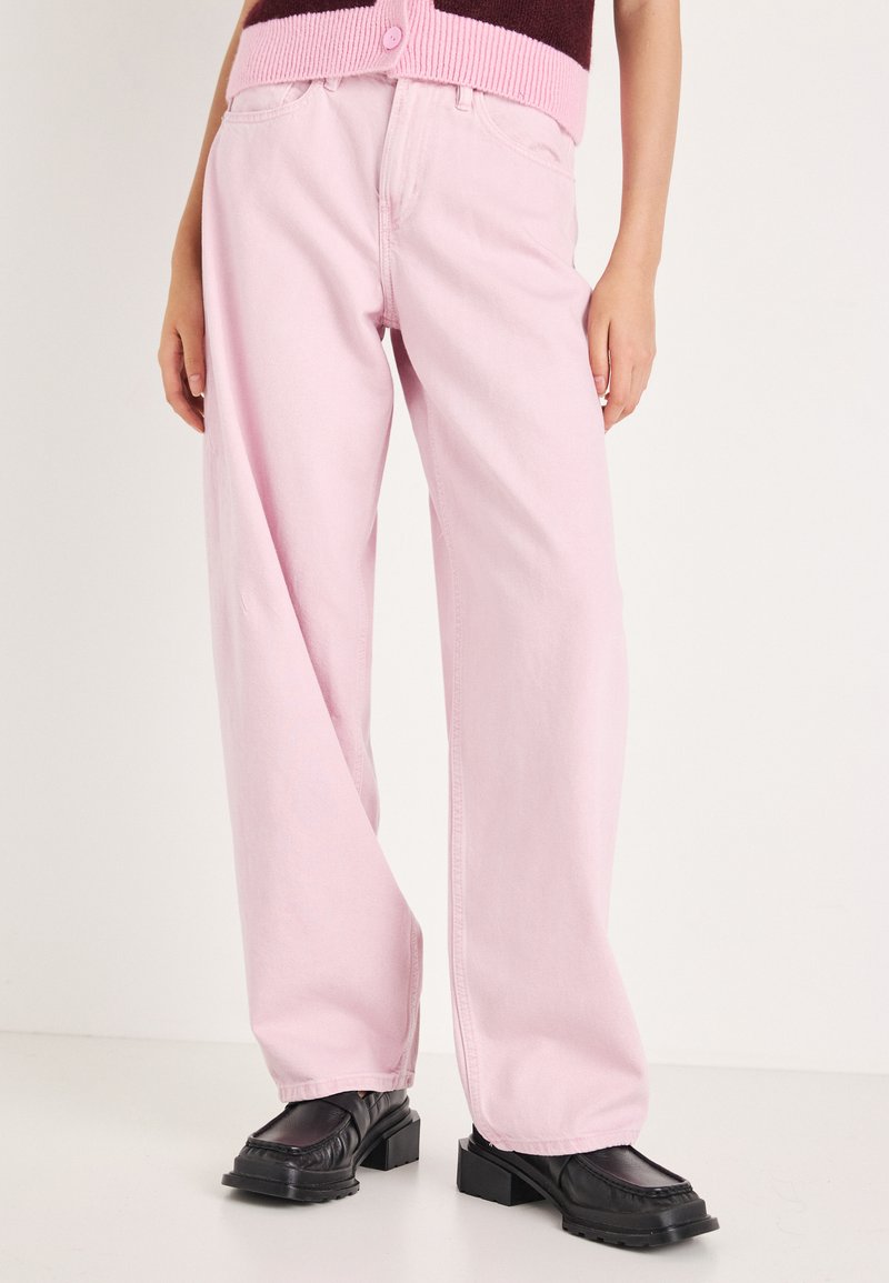 Rozā džinsa platās kājas bikses ar brīvu piegriezumu. Gluda tekstūra. Kombinētas ar melniem apaviem ar reljefa zoli un apaļu purngalu.