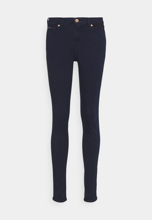 Lieknos džinsai tamsiai mėlynos spalvos, su lygiu paviršiumi, turintys užtrauktuką, dvi priekinės kišenes ir mažą raudoną akcentą prie kišenės krašto.