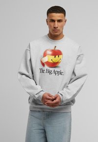 Grå sweatshirt med et stort grafisk motiv af et smilende æble og teksten "The Big Apple" trykt nedenunder, rund halsudskæring og lange ærmer.