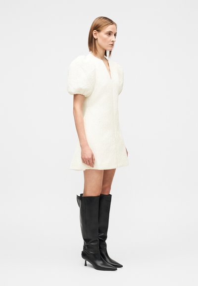 Vestido mini branco texturizado com mangas bufantes e decote em V profundo, combinado com botas pretas de couro até ao joelho, com biqueira pontiaguda.